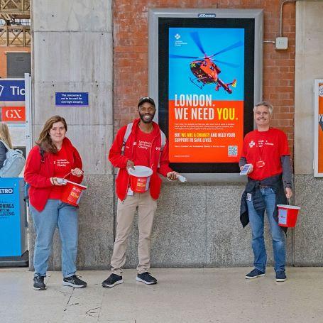 People fundraising in front of an ad for London's Air Ambulance Charity